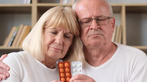 Upset Senior Elderly Couple Holding Pills and Looking at Camera