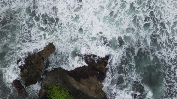 Top down aerial view of giant ocean waves crashing and foaming in coral beach