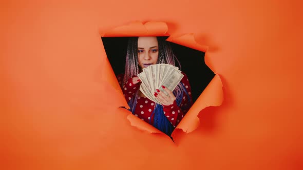 Bright Woman with Money Sticks Out of Hole of Orange Background