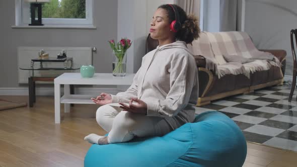 Side View Wide Shot of Relaxed Happy African American Woman Sitting on Bag Chair in Lotus Pose with