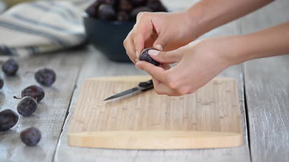 Woman cooking and cutting plum on wooden cutting board. Preparing healthy food.