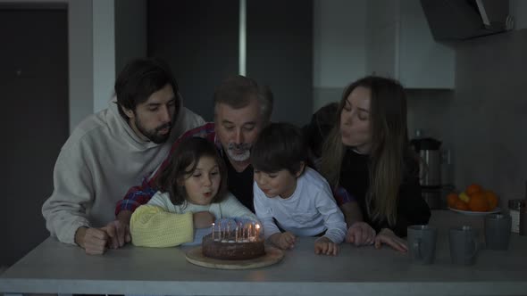 Happy Grandfather Blowing Candles on Birthday Cake Together with His Big Family