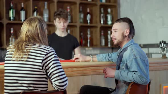 Relaxed Caucasian Men Sitting at Bar Counter Talking and Ordering Drinks with Blurred Young