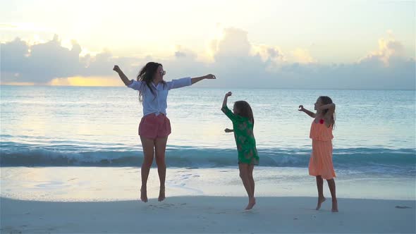 Little Adorable Girls and Young Mother at Tropical Beach in Warm Evening Dancing and Having Fun