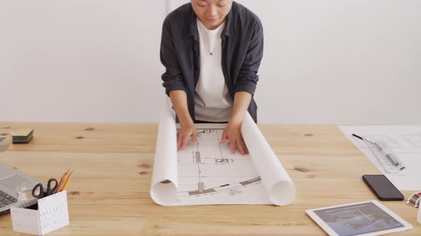 Asian Architect Rolling Out House Plan on Desk