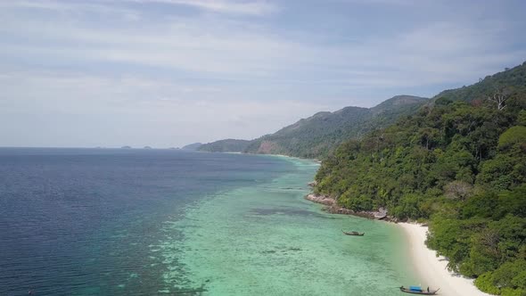 Aerial view of lush island with clear waters and coral reefs by beach in Thailand - camera pedestal