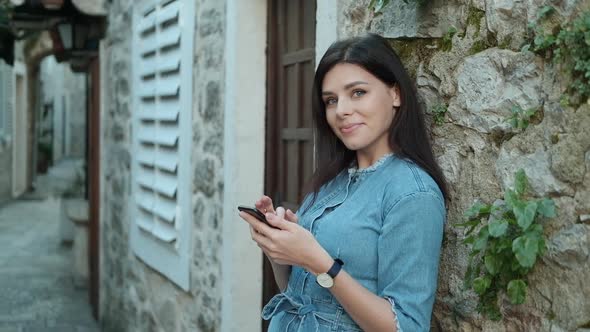 Pretty young woman with brunette hair in denim overalls  texting on her phone