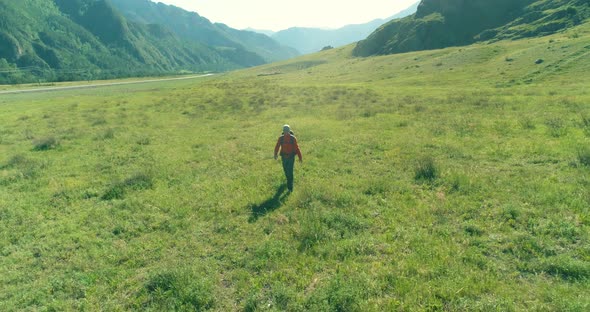 Flight Over Backpack Hiking Tourist Walking Across Green Mountain Field. Huge Rural Valley at Summer