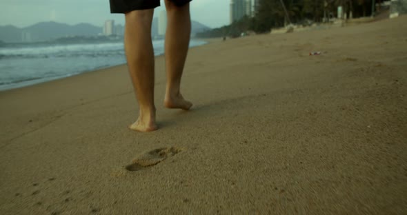 Closeup of the Legs of a Young Caucasian Man Walking on the Sand Along the Shore Outdoors Against