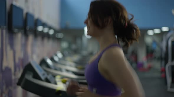 Side View Smiling Slim Caucasian Young Woman Jogging on Treadmill in Gym Indoors