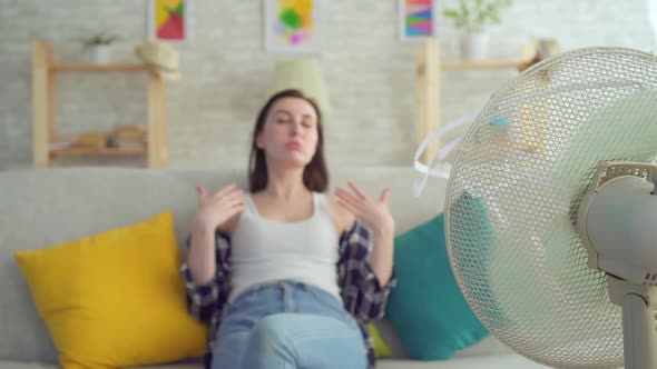 Young Woman Sitting on a Sofa with an Electric Fan Escapes From the Heat