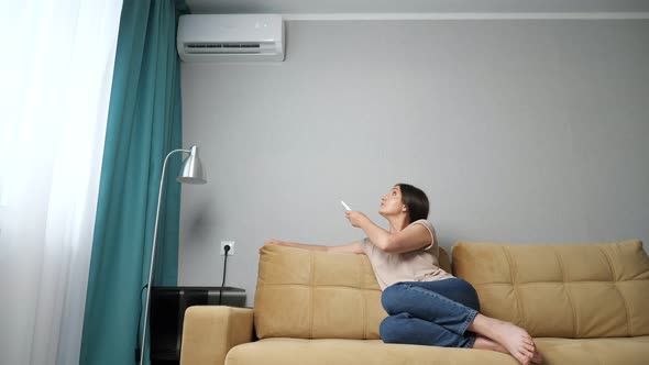 Brunette Woman Turns on the Air Conditioner While Sitting on the Couch