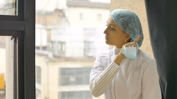 Portrait of Unhappy Tired Young Doctor Eating an Apple Near a Window