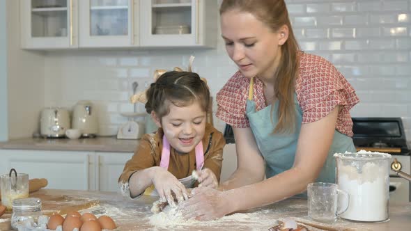 Happy Mother and Daughter Cook Together in the Kitchen, Knead the Dough. The Daughter Laughs and