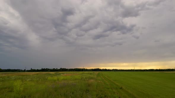 Closeup flight over green summer field in Munich, Germany. Dramatic sky with storm clouds at sunset.