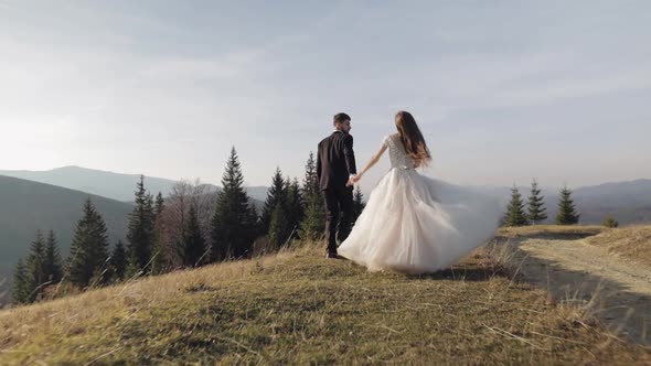 Newlyweds. Caucasian Groom with Bride Running on Mountain Slope. Wedding Couple
