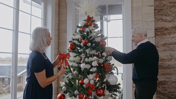 Grandparents Decorating Christmas Tree and Laughing in Big and Bright House