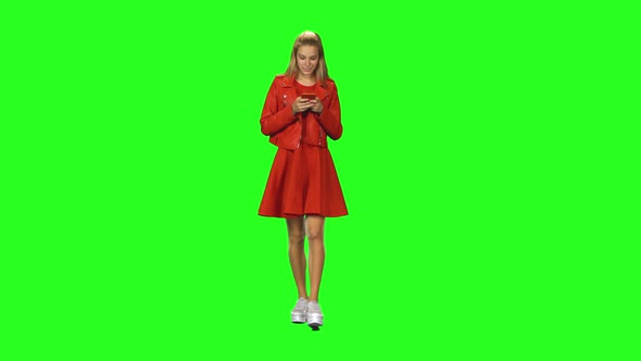 Blonde Girl Is Calmly Walking and Reading Text Message on Her Mobile Phone at Green Screen. Chroma