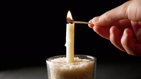 Hand Lights White Wax Candle Using a Match on a Black Background