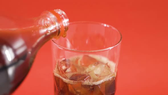 Close-up, pouring cola into glass with ice.