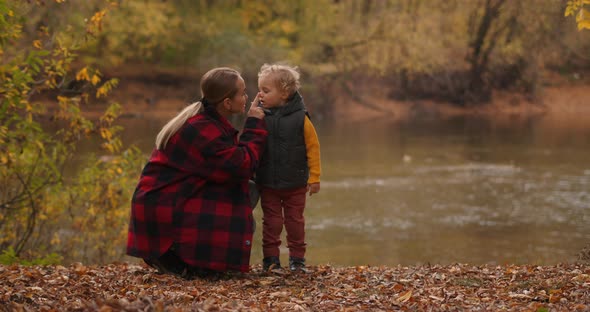 Woman Is Playing with Her Toddler in Forest, Resting on Shore of Lake at Autumn Day, Happy Family