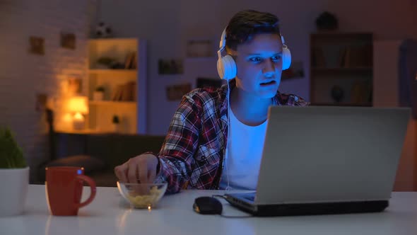 Overemotional Teen Playing Computer Game on Laptop and Eating Snacks, Addiction