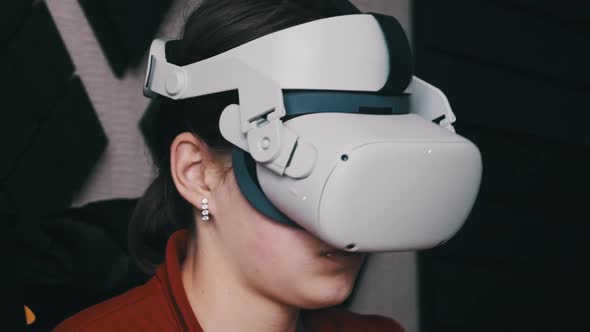 Young Woman in VR Helmet Sitting on Sofa and Communicating in Virtual World