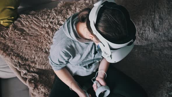 Young Woman in Virtual Reality Helmet Sitting on Sofa and Move Hands at Home