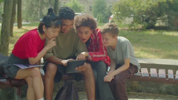 Multiracial College Students with Tablet Pc Checking Exam Results on Bench
