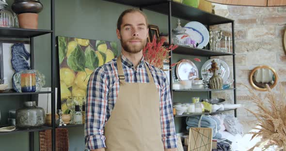 Young Bearded Shopworker in Apron Looking at Camera with Crossed Arms