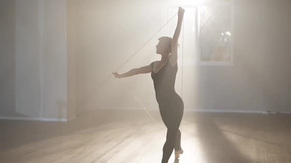Side View of Confident Concentrated Hardworking Ballerina Rehearsing Movements in Backlit Fog in