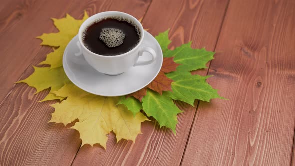 Coffe Cup on Wooden Table with Colorful Autumnal Maple Leaves with Spinning Coffee Bubbles