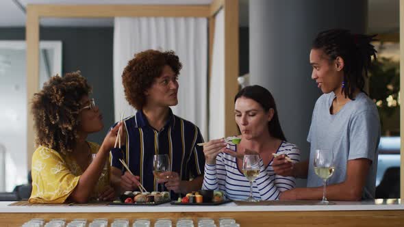 Diverse group of happy friends drinking wine eating sushi and talking at a bar