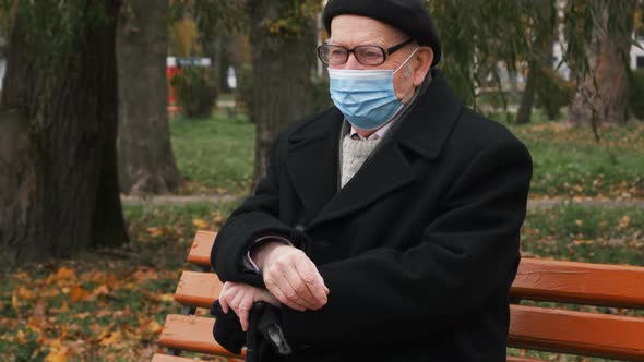 Pandemic concept. Elderly senior sitting outside on bench in park at autumn.