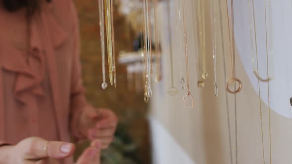 Close up of hand of caucasian woman touching golden necklaces hanging on rack, shopping for jewelry