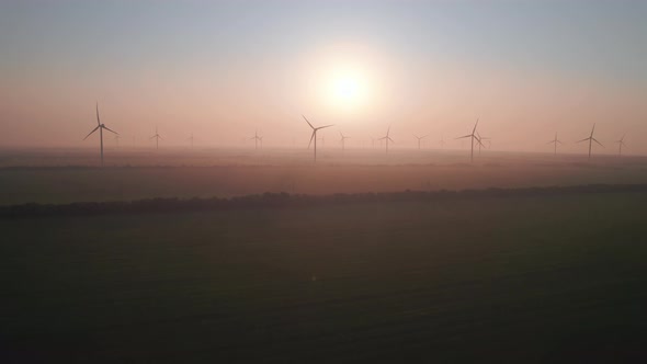 Windmills with rotating wings at sunset or sunrise.