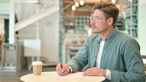 Serious Middle Aged Man Writing on Paper in Cafe 