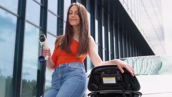 A Girl Stands with Charger Near Her Electric Car