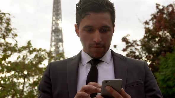 Businessman in a Suit Looks at His Phone on the Background of the Eiffel Tower