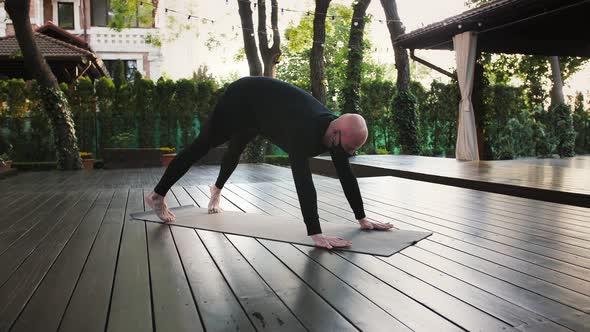 Athletic Bald Male in Black Protective Mask and Sportswear is Performing Yoga on Mat and Wooden