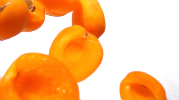 Ripe Juicy Apricot Halves are Falling Diagonally on a White Background