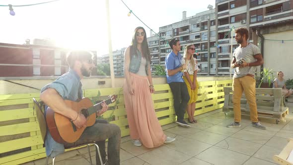 Friends having fun on the rooftop terrace, playing guitar and taking photos