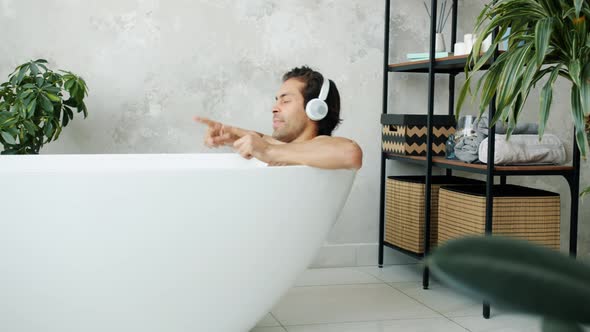 Happy Young Man Dancing Taking Bath Wearing Wireless Headphones and Listening To Music