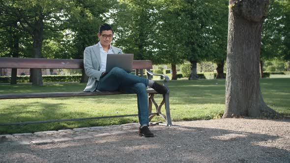 Korean Businessman On Park Bench Using Laptop