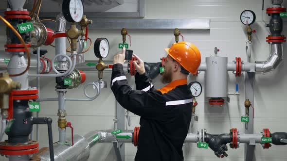 A Worker at a Factory Checks the Readings of Pressure Gauges on the Pipeline Uses a Smartphone to