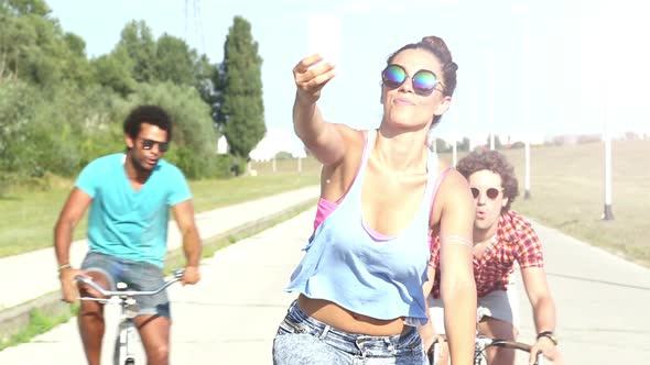 Three young adults having fun cycling and taking selfies, graded