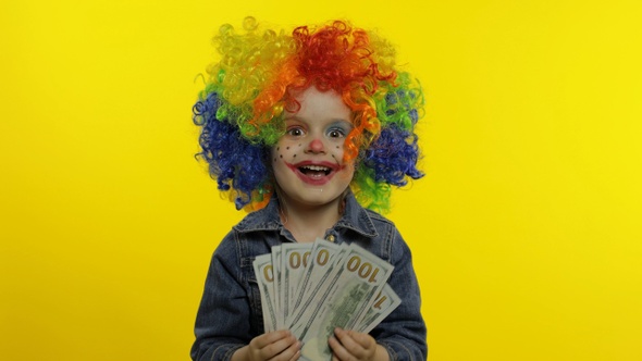 Child Girl Clown in Colorful Wig Making Silly Faces with Money Banknotes Dollar Cash. Halloween