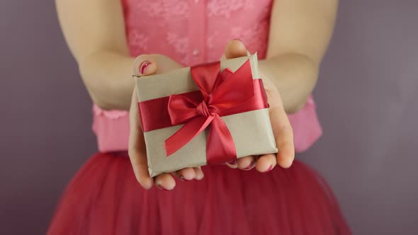 Wrapped little gift box with red ribbon bow in female hands. Present for Valentines Day or Christmas