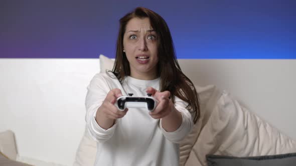 Joyful Attractive Woman in White Pajamas Plays Video Games with Joystick in Bed