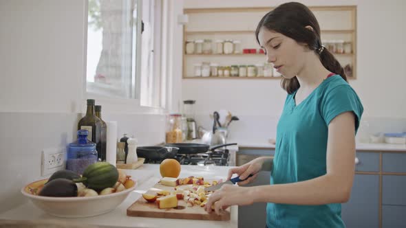 Teenage girl working cutting fruit for breakfast in the kitchen